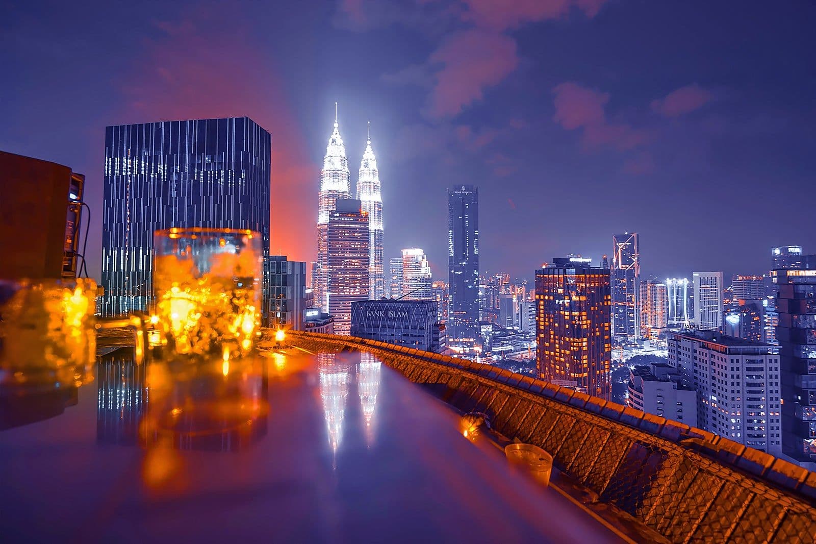 Candlelit drinks on the ledge of a rooftop bar at night, with the illuminated Petronas Twin Towers and the Kuala Lumpur skyline beyond