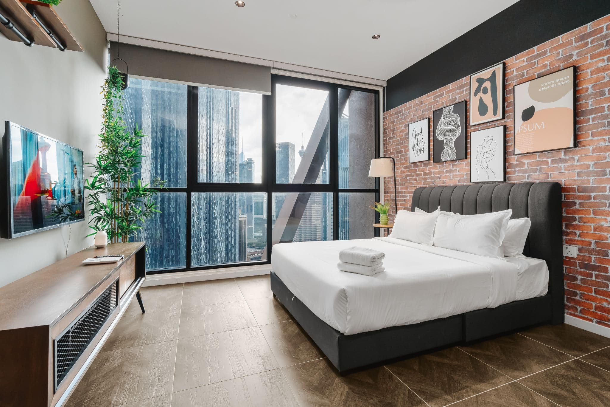 Bedroom of a managed short-stay apartment in Kuala Lumpur, hotel-made bed and folded towels, floor-to-ceiling windows facing the city skyline